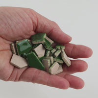 Video of Flip ceramic puzzle pieces in moss green, opaque glazed porcelain, 4–20 mm, held in a hand and poured out to show their shapes and finish