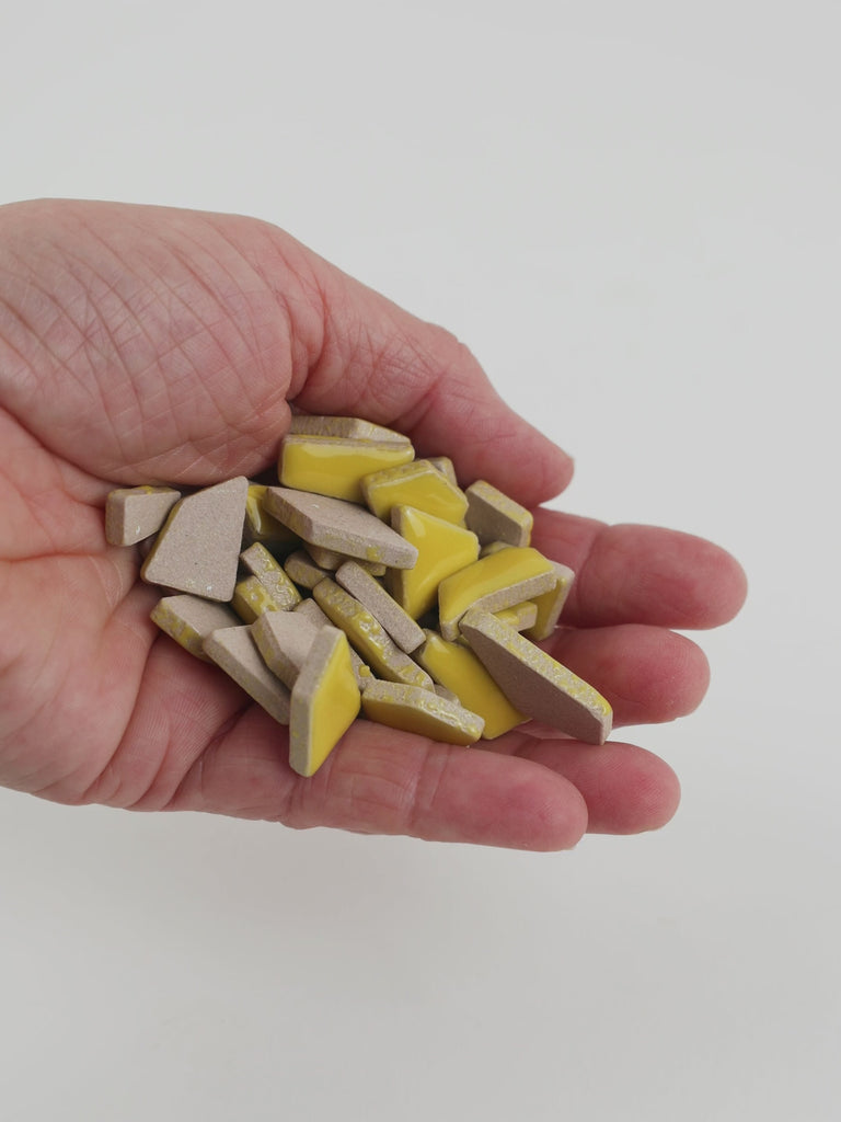 Video of Flip ceramic puzzle pieces in corn, opaque glazed porcelain, 4–20 mm, held in a hand and poured out to show their shapes and finish