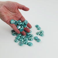 Video of opal cyan glass nuggets, opaque with a pearly iridescent sheen, 16–20 mm, picked up from a pile by hand and dropped back to show their size, round shape and shine