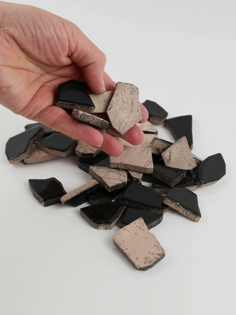 Video of Flip XL ceramic puzzle pieces in black, opaque glazed porcelain, 20–60 mm, picked up from a pile by hand and dropped back to show their size, shapes and finish