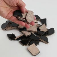 Video of Flip XL ceramic puzzle pieces in black, opaque glazed porcelain, 20–60 mm, picked up from a pile by hand and dropped back to show their size, shapes and finish