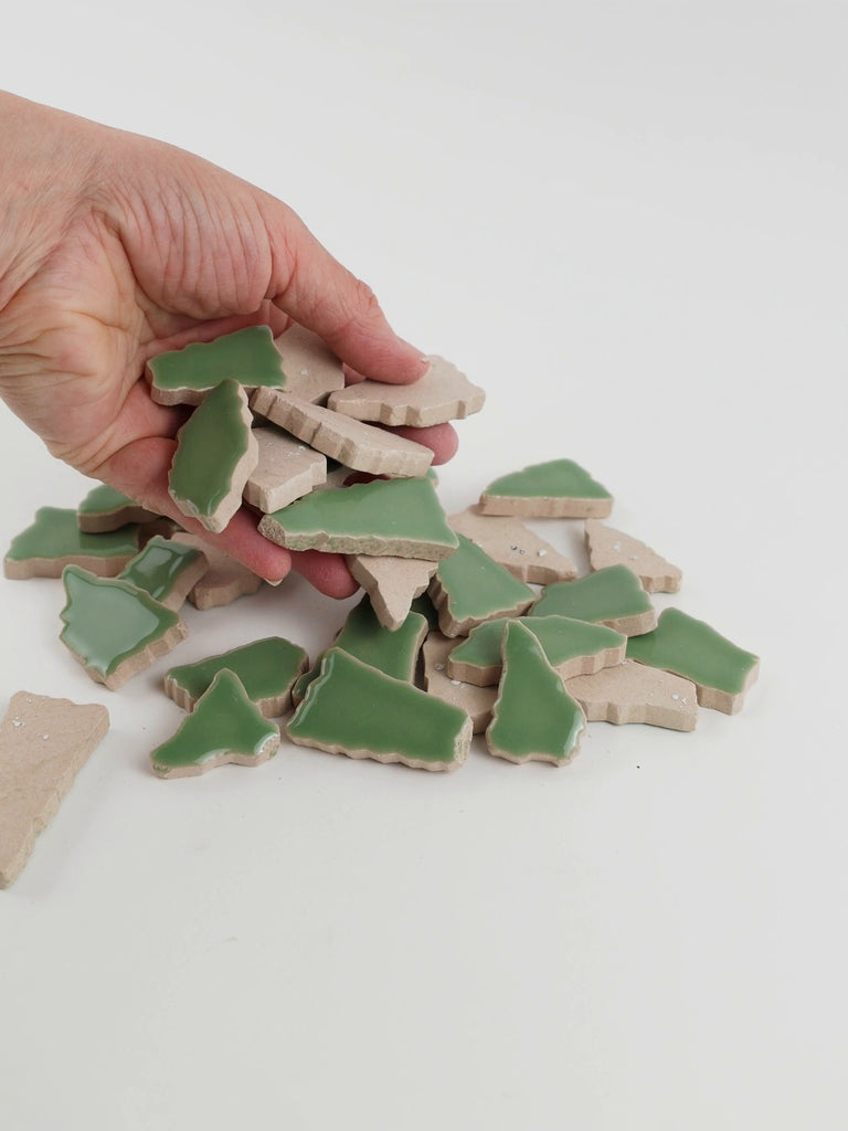 Video of Flip XL ceramic puzzle pieces in reed green, opaque glazed porcelain, 20–60 mm, picked up from a pile by hand and dropped back to show their size, shapes and finish
