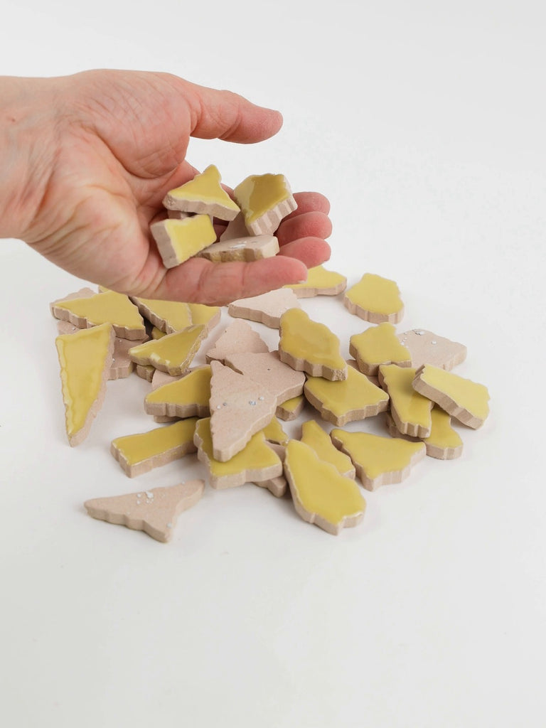 Video of Flip XL ceramic puzzle pieces in ochre yellow, opaque glazed porcelain, 20–60 mm, picked up from a pile by hand and dropped back to show their size, shapes and finish