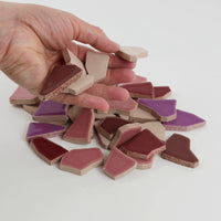 Video of Flip XL ceramic puzzle pieces in purple mix, opaque glazed porcelain, 20–60 mm, picked up from a pile by hand and dropped back to show their size, shapes and finish