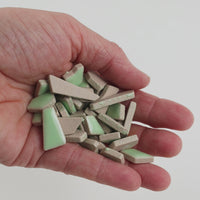 Video of Flip ceramic puzzle pieces in linden green, opaque glazed porcelain, 4–20 mm, held in a hand and poured out to show their shapes and finish