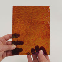 Video of the Amber Hammered iridescent glass plate in transparant amber, 15x19cm, held up and tilted to show its pattern and transparency